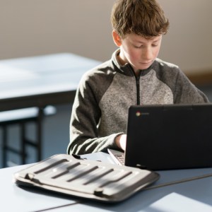 student using a chromebook with a device bag next to it