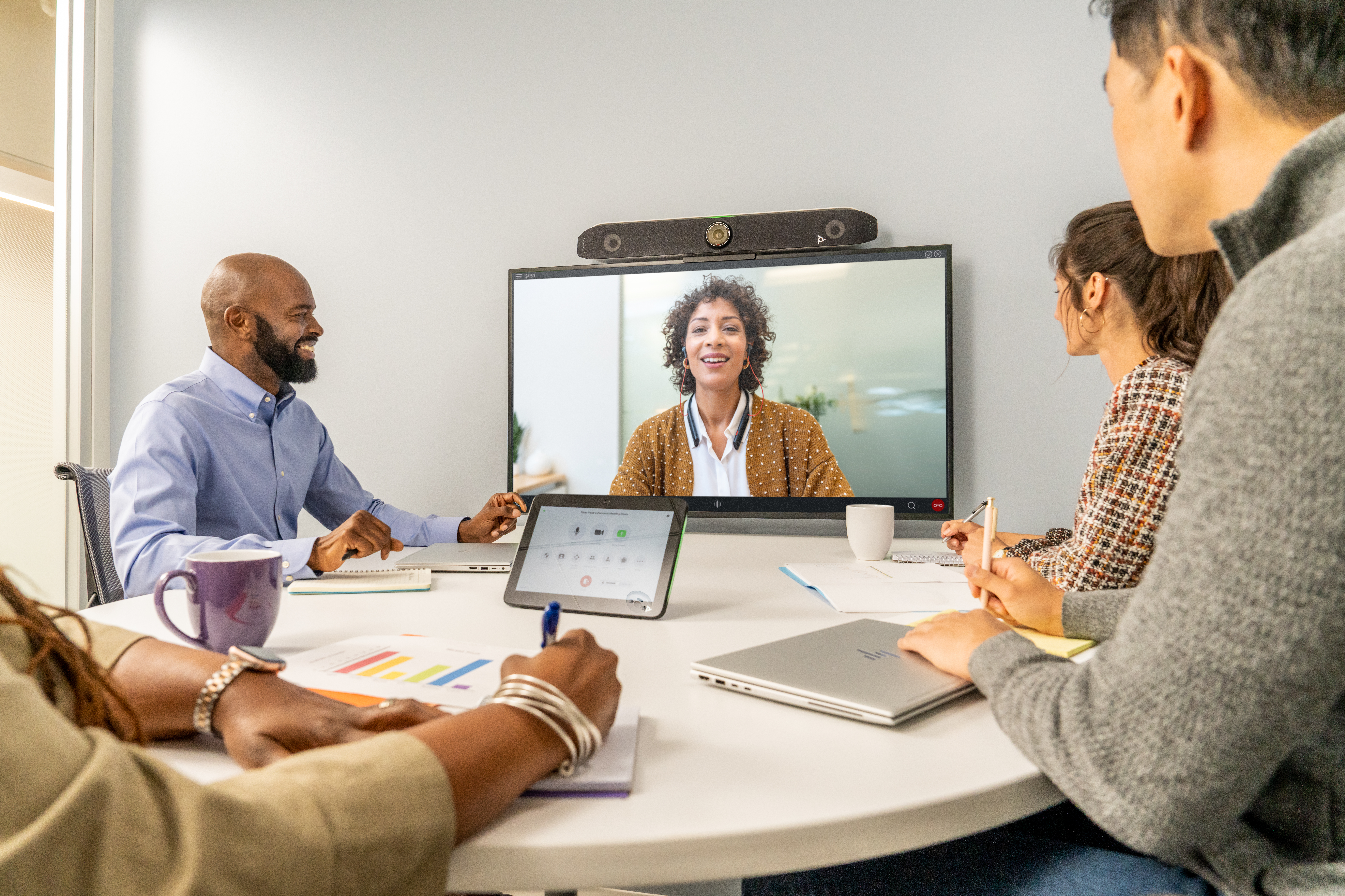 employees gathered together in a conference room talking to a person on a video screen